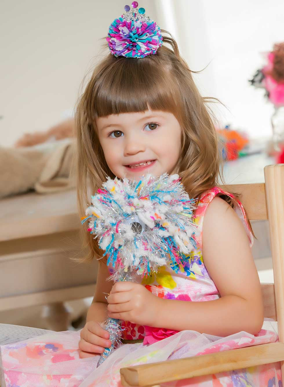 Little girl sitting in a chair with HappyHappy hair clip in her hair and Happy Monster wand